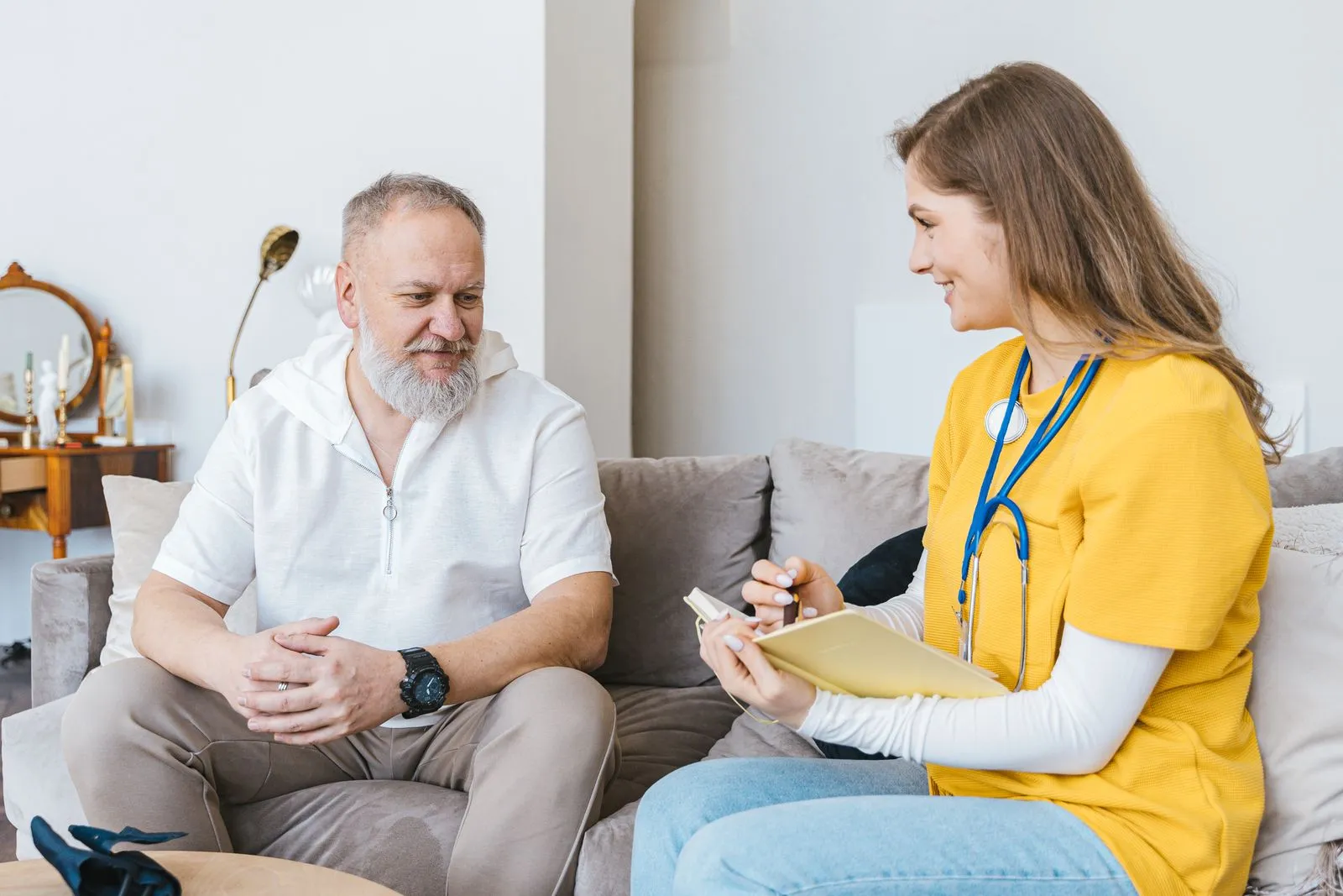 A nurse in scrubs taking notes while talking with an older resident
